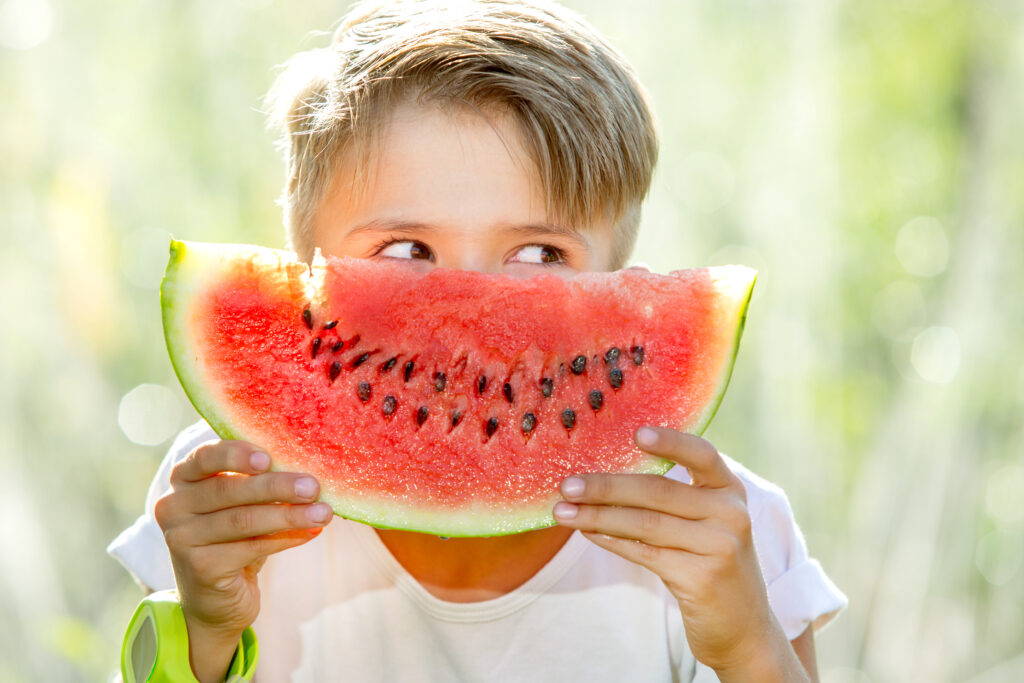 Little Boy Holding Watermelon In Front of Mouth