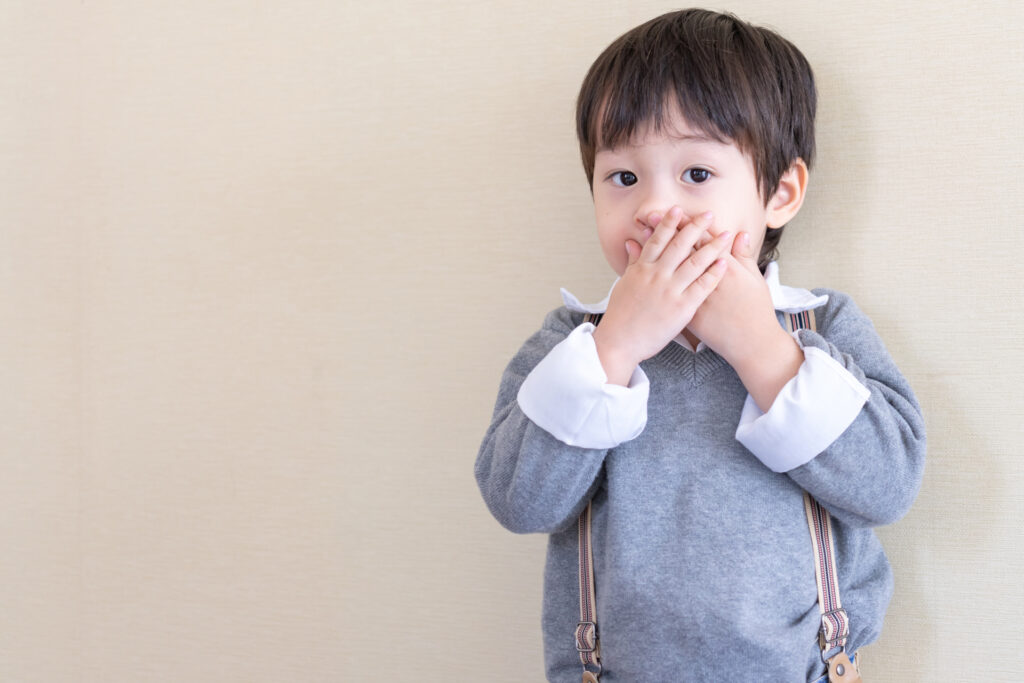 Young Boy Holding Hands Over Mouth