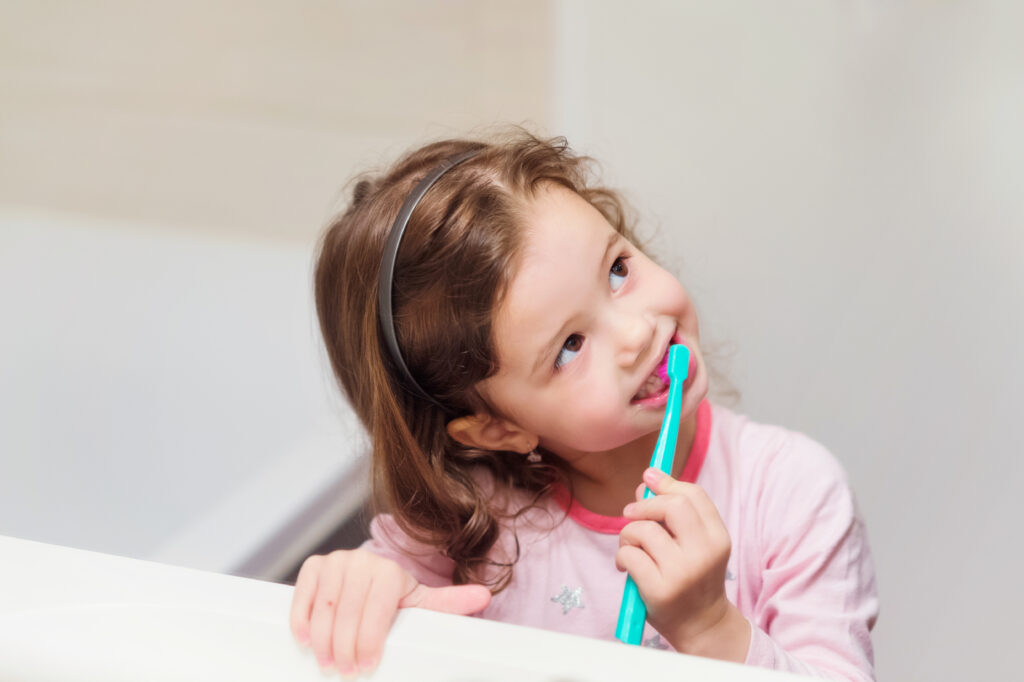 Little girl brushing her teeth with a blue toothbrush
