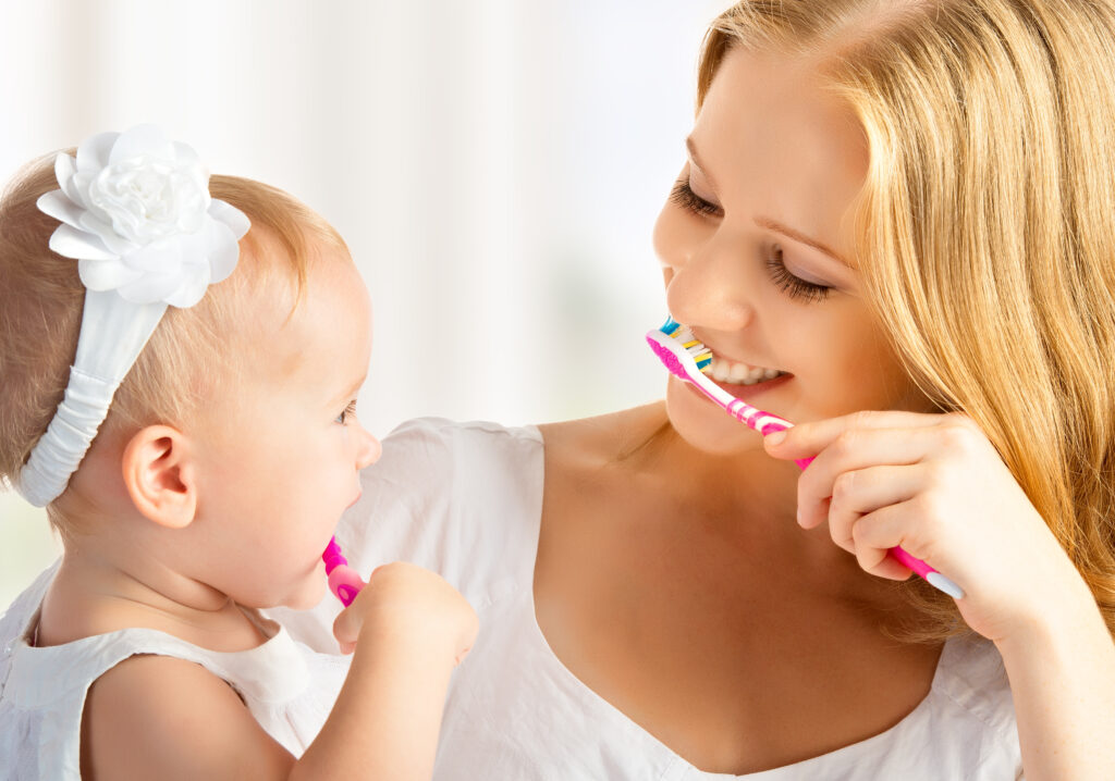 Mom and baby brushing their teeth together with pink toothbrushes 